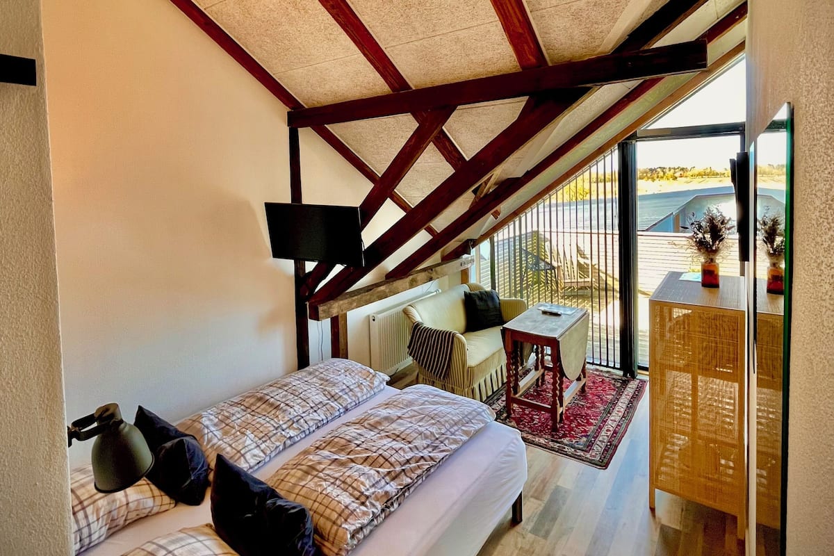 Ein Schlafzimmer mit einem großen Bett, einem kleinen Tisch und Blick ins Freie.