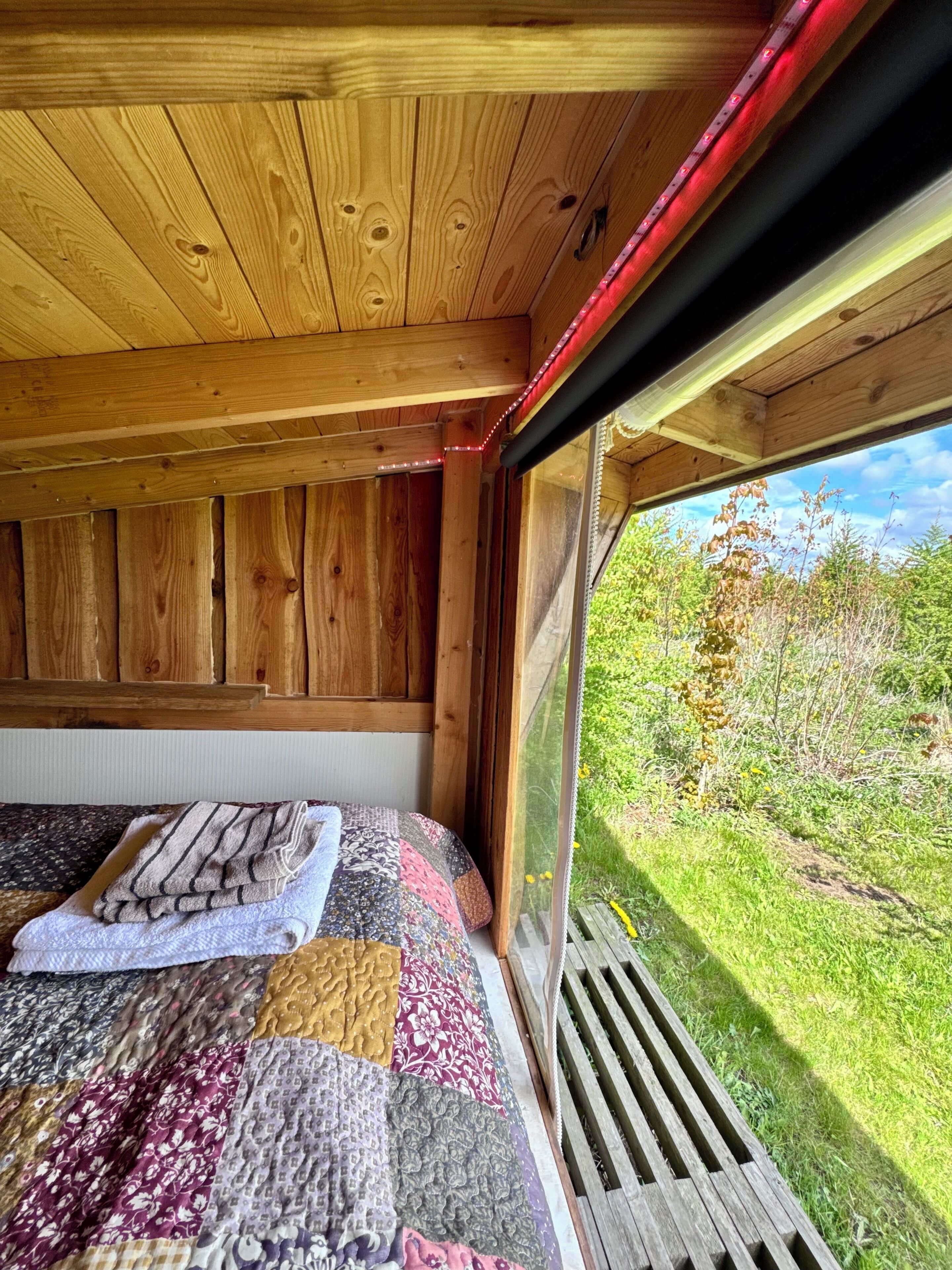 L’intérieur d’une cabane en bois, avec un lit, une fenêtre et une vue sur la verdure environnante.