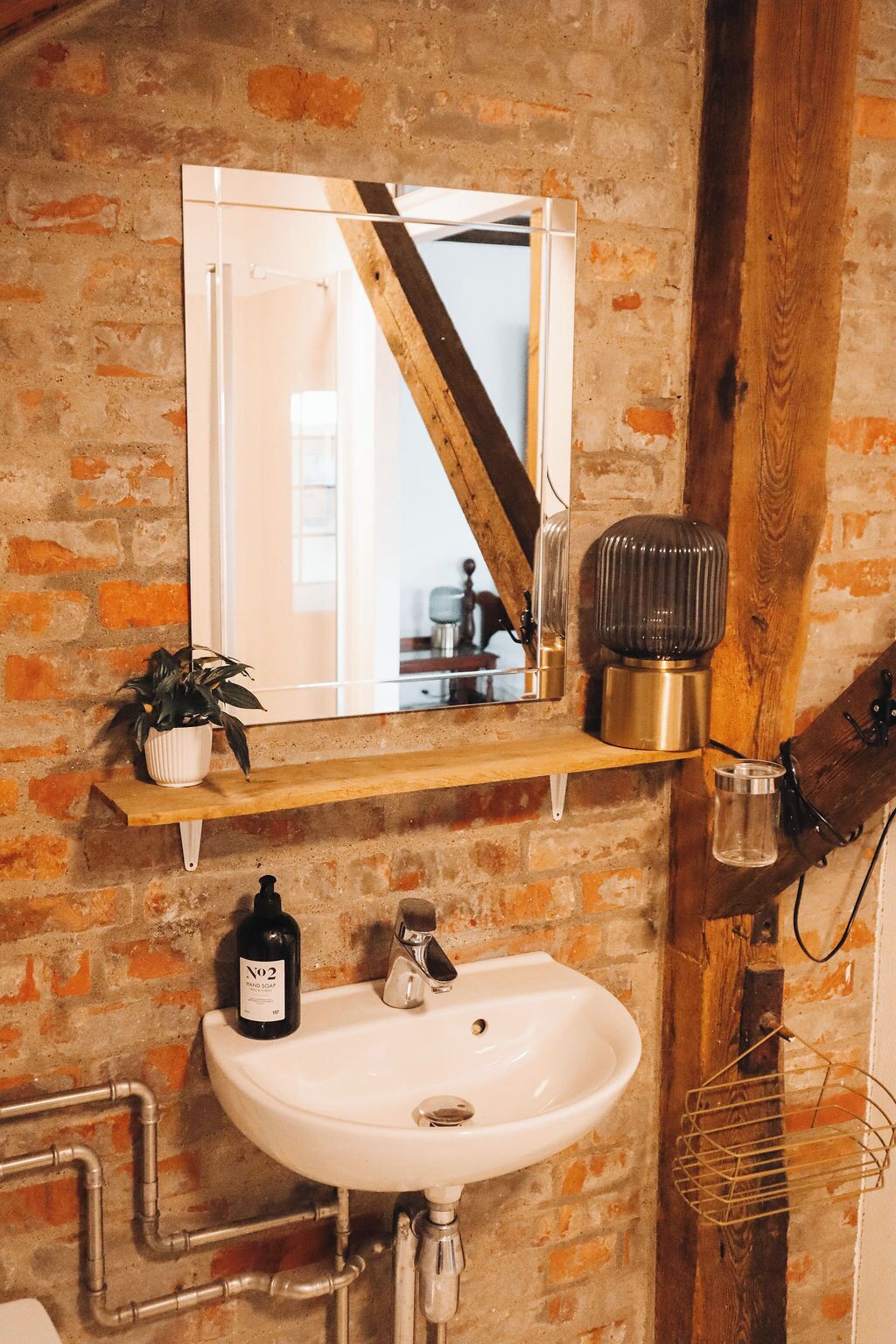 Ein Badezimmer mit einem weißen Waschbecken, einem Spiegel und einem Regal mit einem Topfpflanzen.