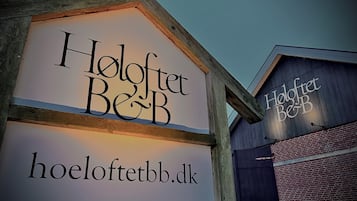 A wooden sign with the text "Hooflet Be&B" and a website address "hoofletbb.dk".