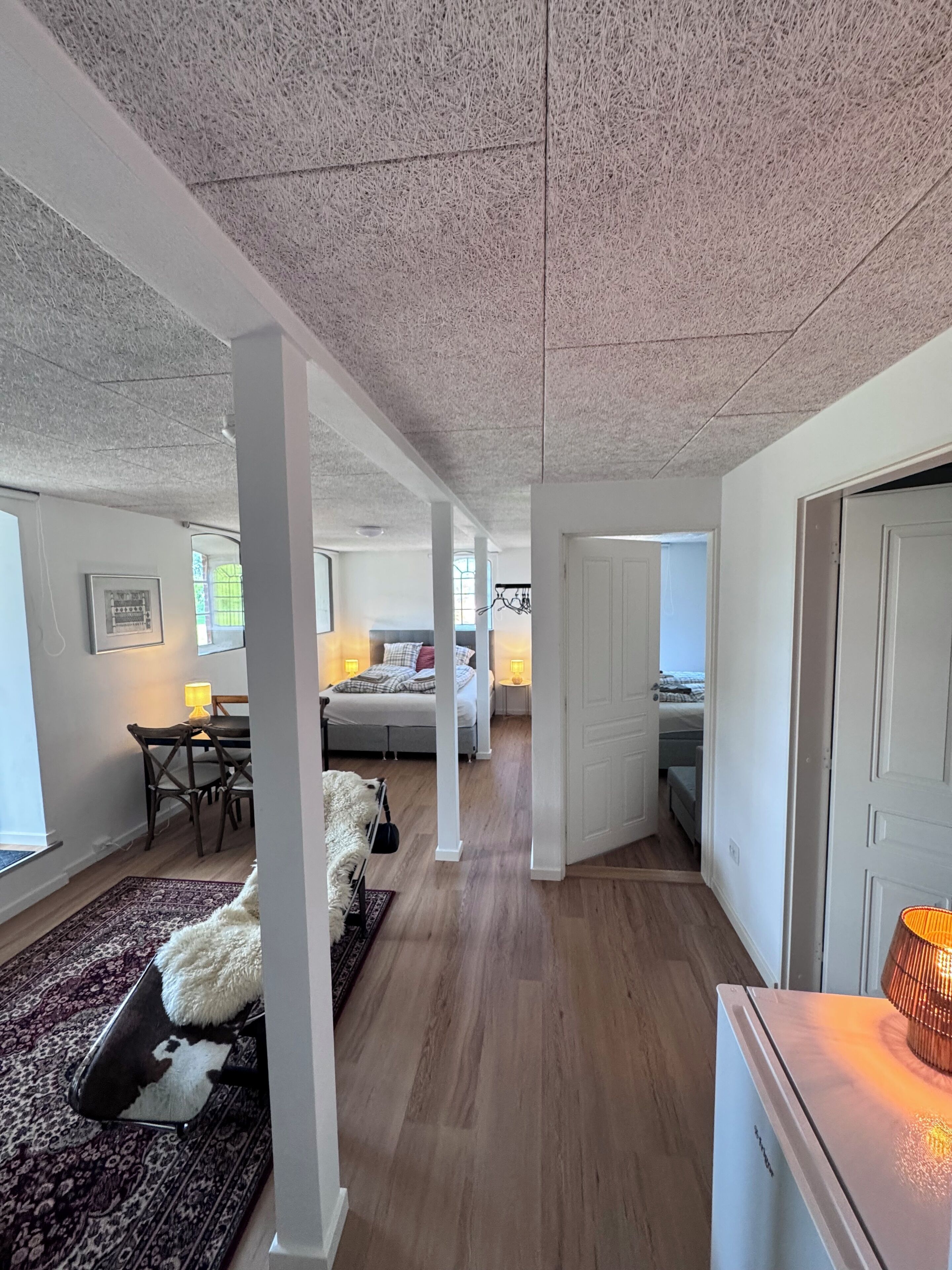 Un interior moderno con un pasillo que conduce a dormitorios, un comedor y una sala de estar con sofá y alfombra.