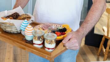 A person holding a tray with various food items, including fruits, cheeses, and pastries.