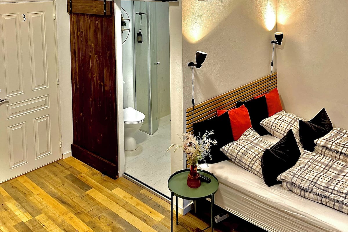 Ein Schlafzimmer mit Bett, Nachttisch, Fenster und Tür.