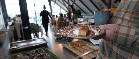 Una persona sosteniendo un plato con un postre y una taza, con una bandeja de brownies y una tabla de cortar con un cuchillo sobre una mesa en un restaurante.