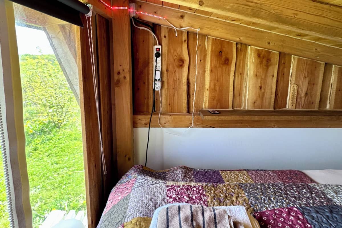 Ein Holzinnenraum mit Bett, Fenster und Steckdose.