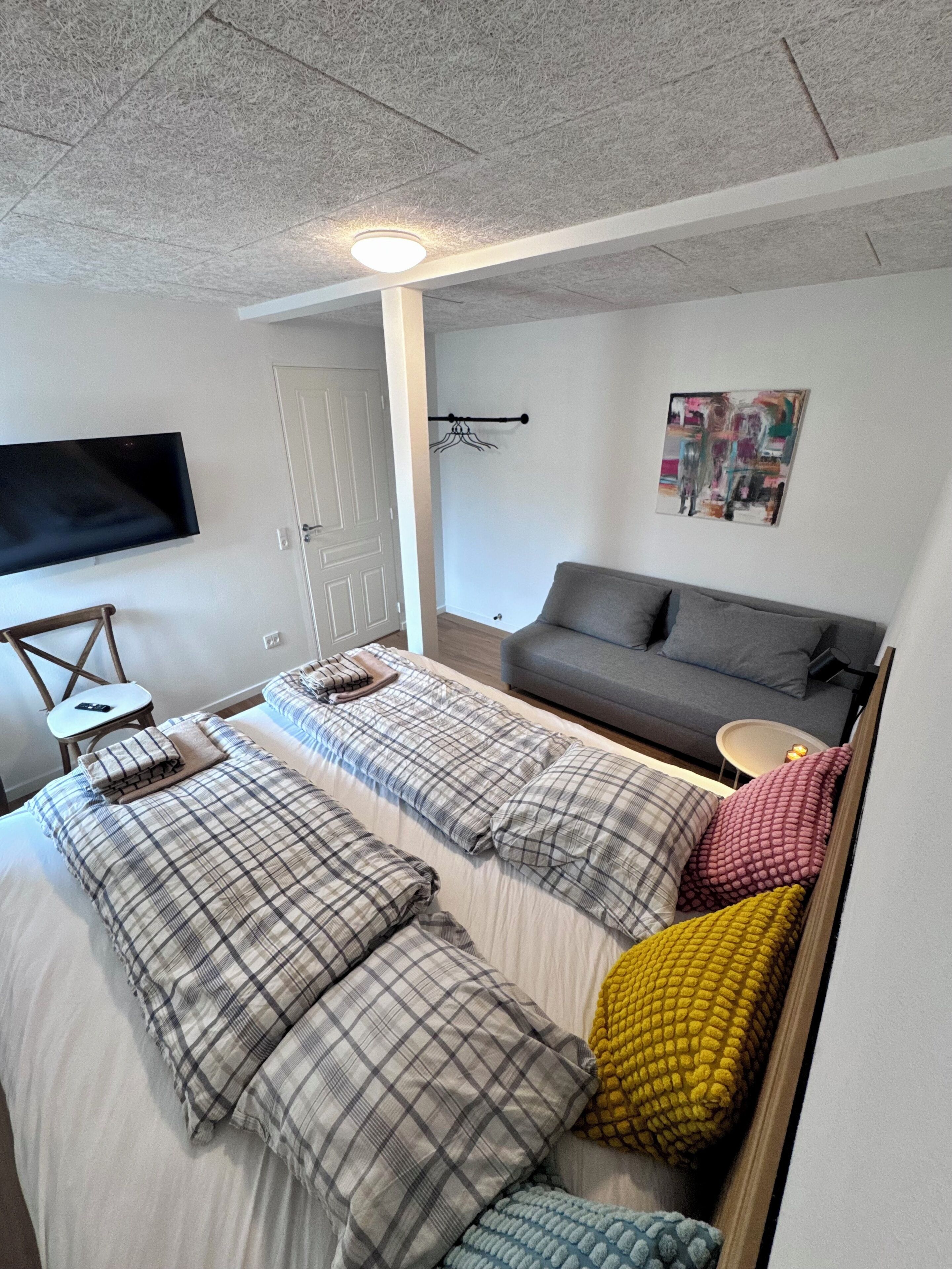Een kamer met twee bedden, een bank, een flatscreen televisie, een deur en een kunstwerk aan de muur.