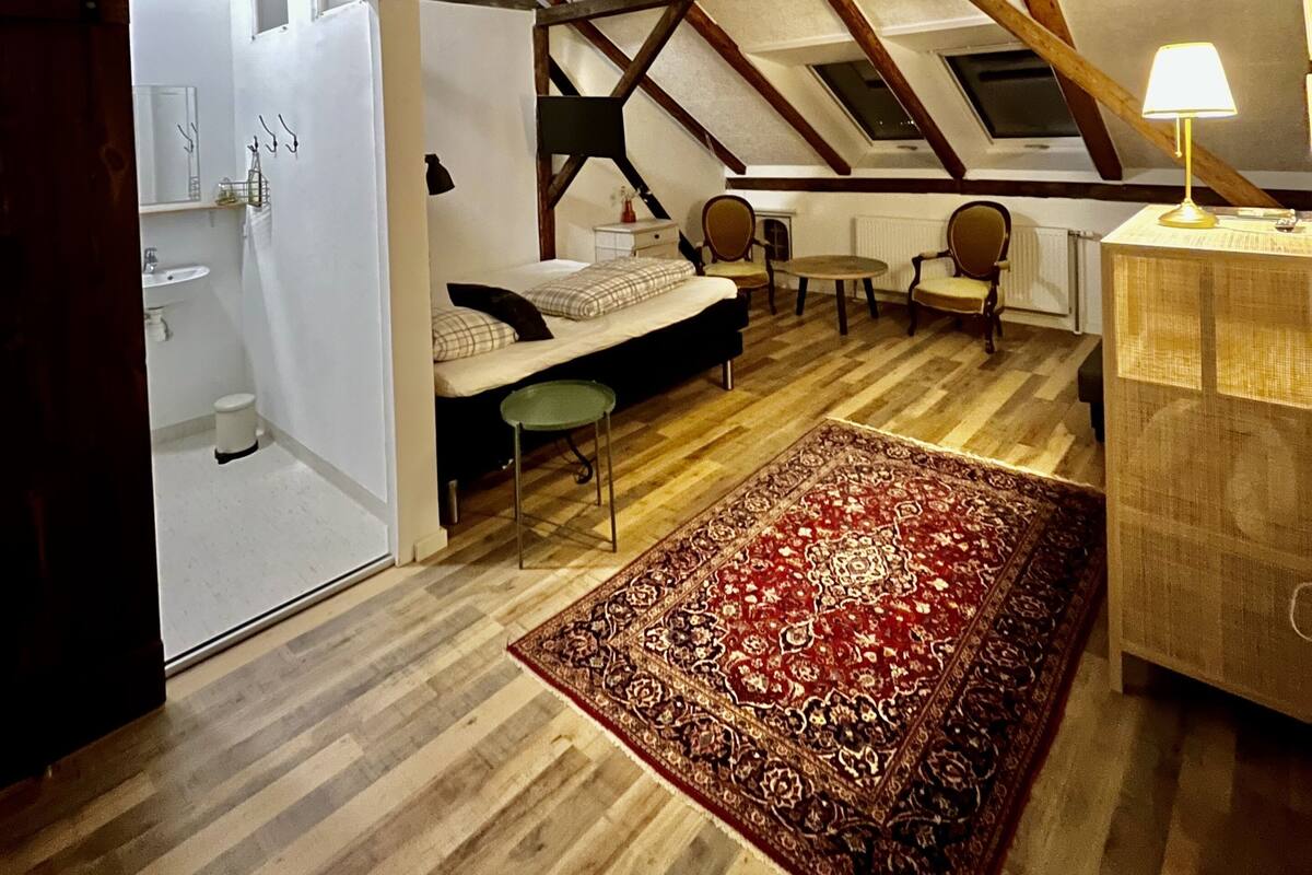 Ein Schlafzimmer im Loft-Stil mit Schräge, einem Bett, einem Schreibtisch und einem Stuhl.