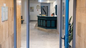 Un couloir menant à un espace d’accueil comprenant un comptoir, une plante et une porte.