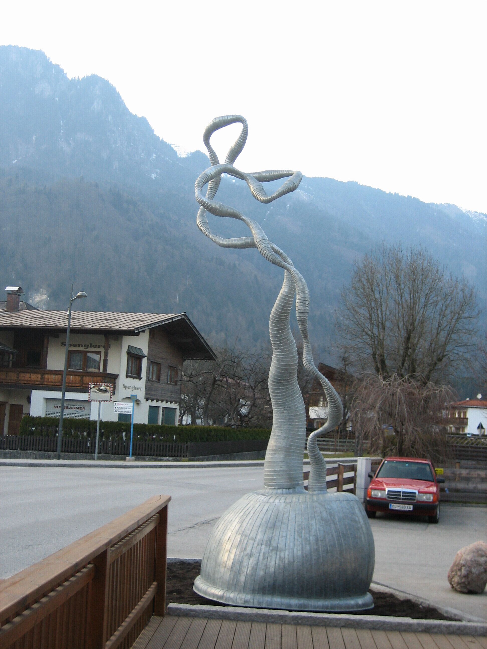 Una escultura de metal en una plaza pública con montañas al fondo.