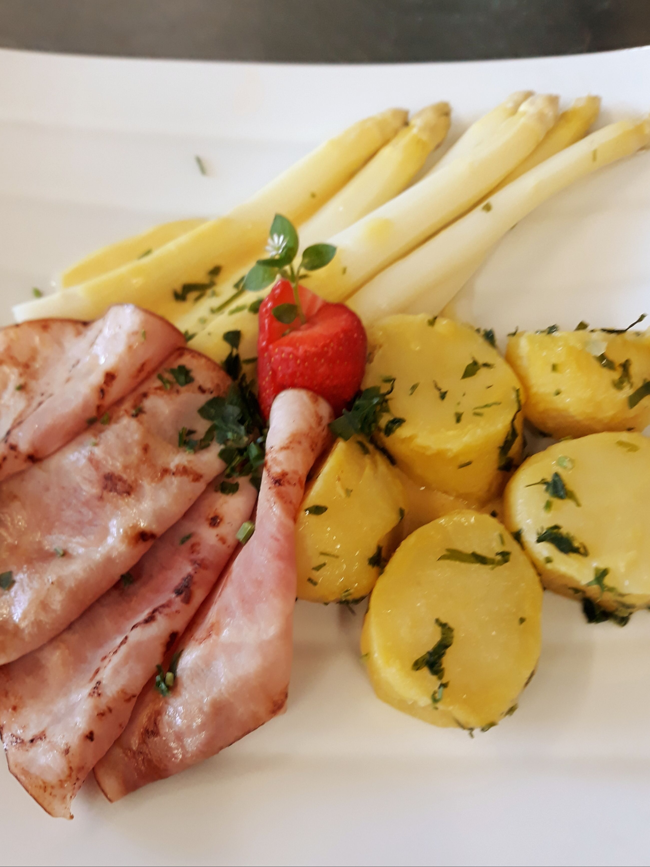A plate with grilled ham, asparagus, potatoes, and a strawberry garnish.
