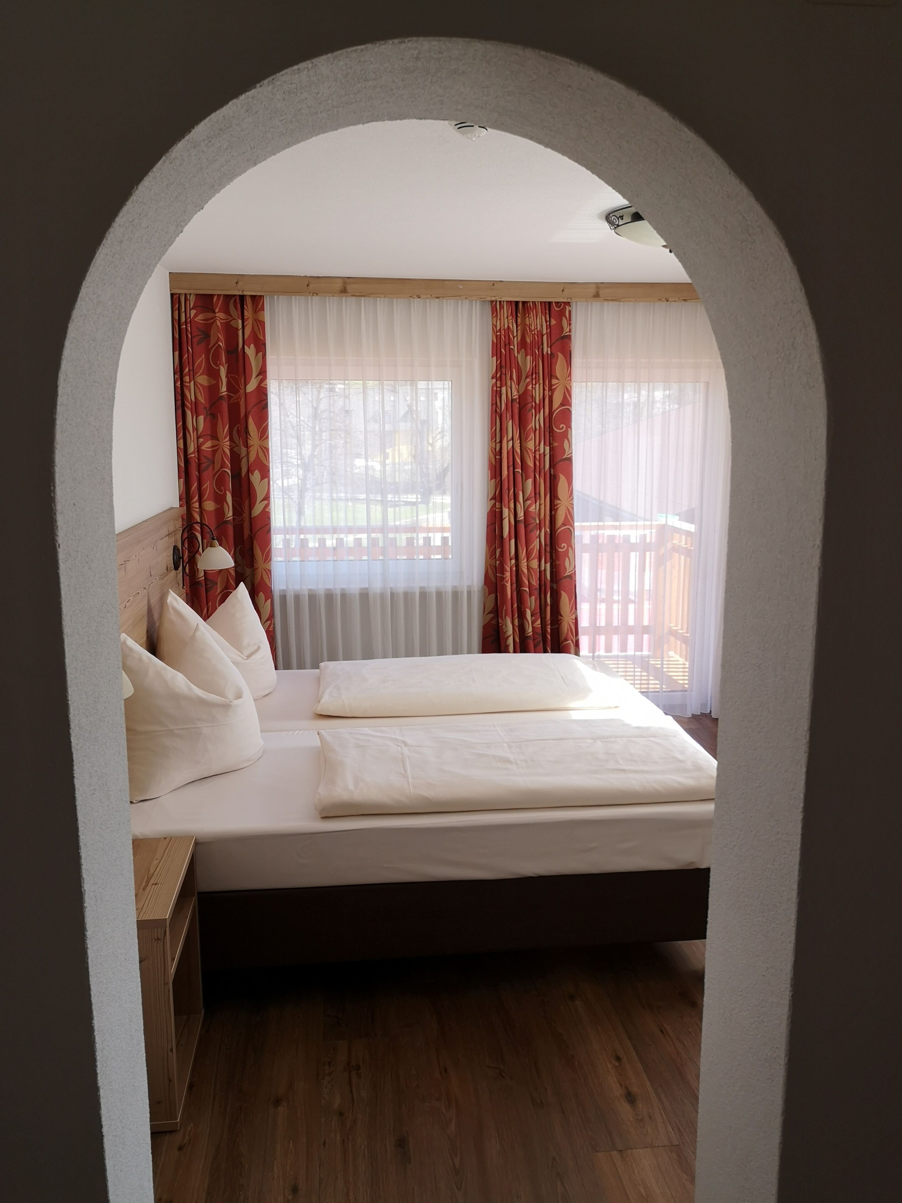 Un dormitorio con cama, almohadas, una mesita de noche y una ventana con cortinas.