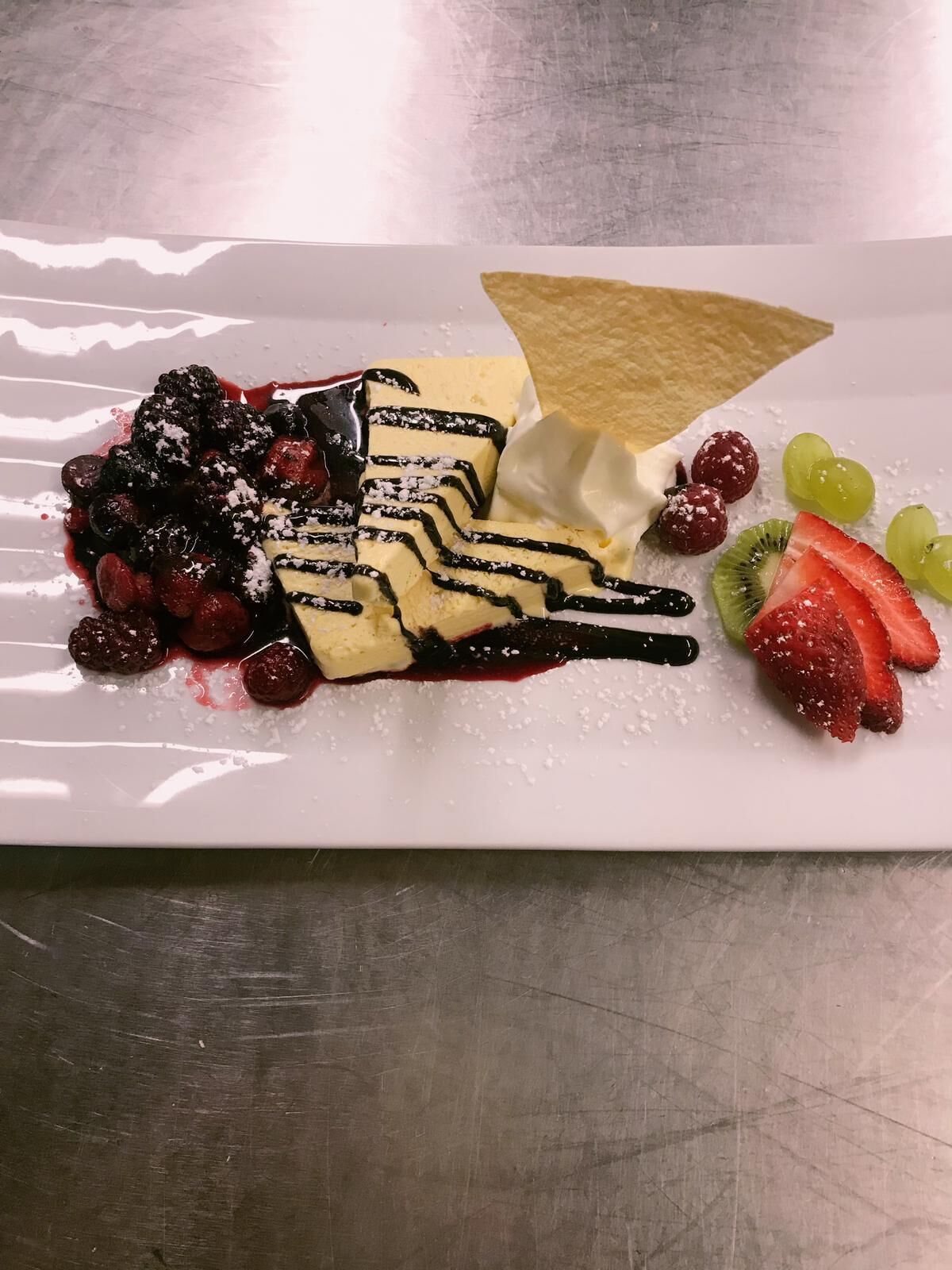 Un plato de postres con varias frutas y un chorrito de chocolate.
