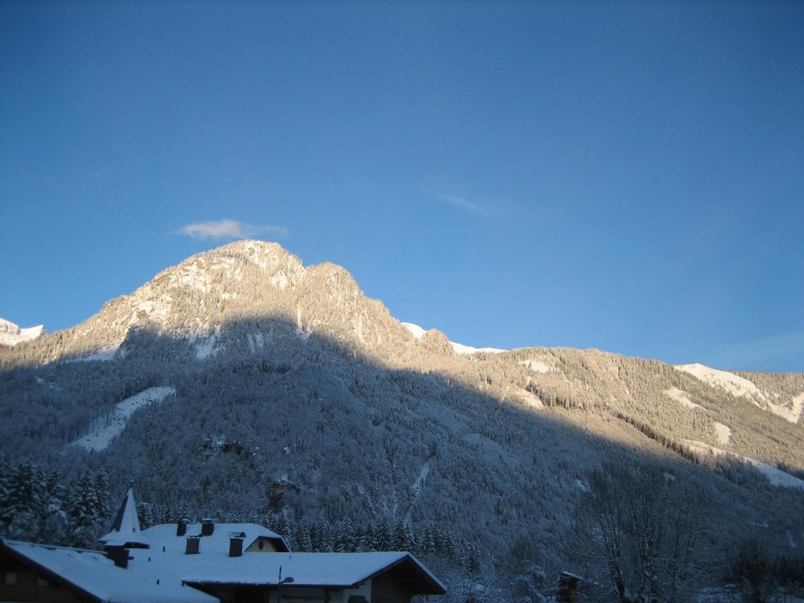 A mountain with a snow-covered peak and a building with a sloped roof in the foreground.