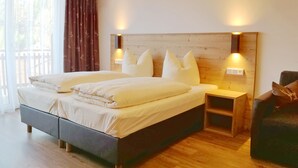 Ein Schlafzimmer mit Holzboden, einem Bett mit weißer Bettwäsche, zwei Nachttischen mit Lampen und Blick ins Freie durch ein Fenster.