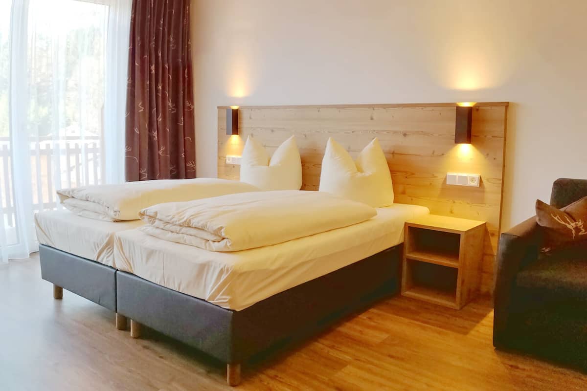 A bedroom with a wooden ceiling, a bed with white bedding, two bedside tables with lamps, and a view of the outdoors through a window.