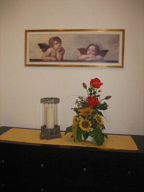 Un cuadro enmarco con querubines sobre una mesa con un jarrón de girasoles y un candelabro.