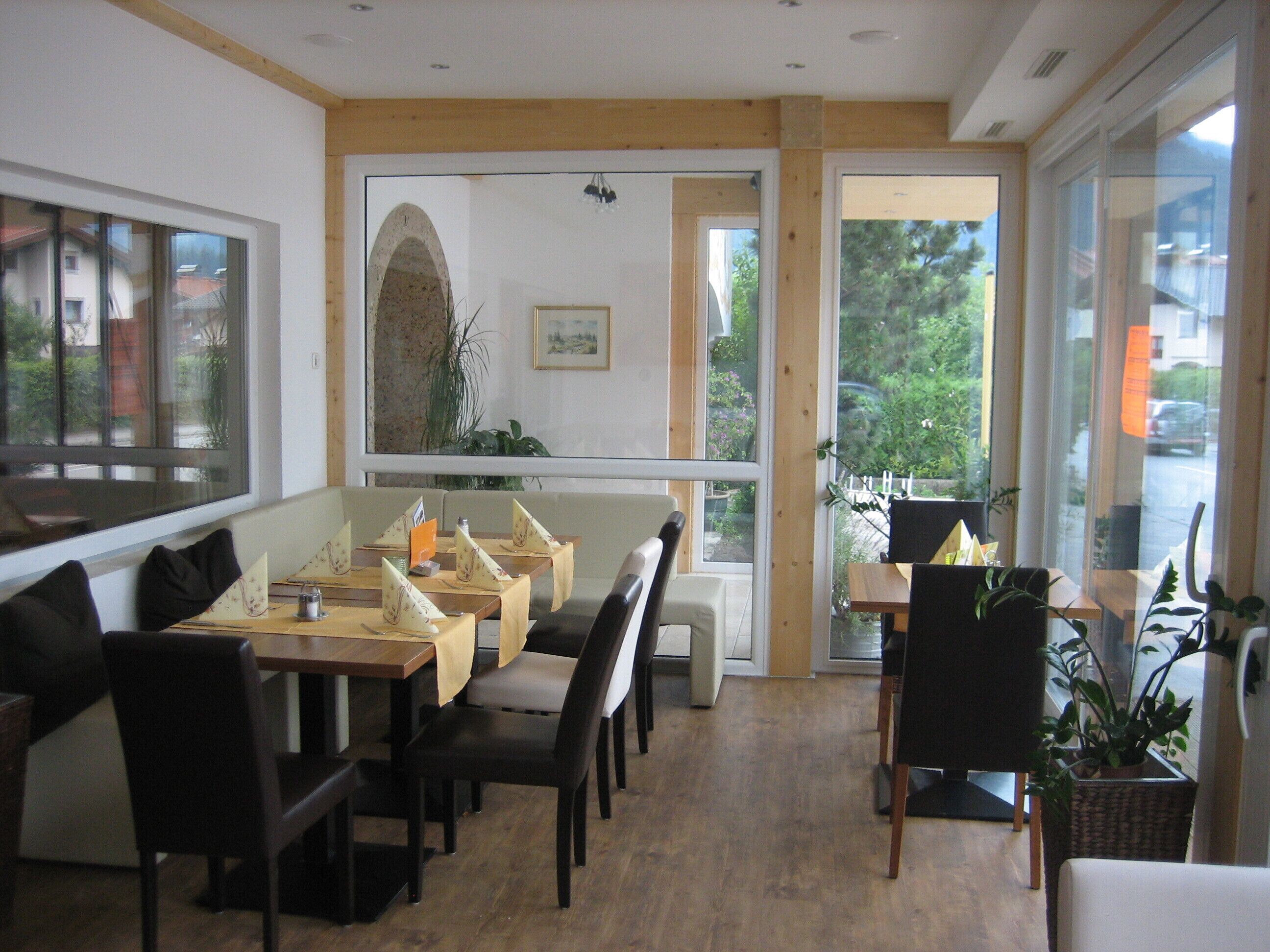 A restaurant with a long counter, multiple tables, and chairs. There are large windows providing a view of the outside.