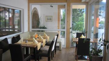 A restaurant with a long counter, multiple tables, and chairs. There are large windows providing a view of the outside.