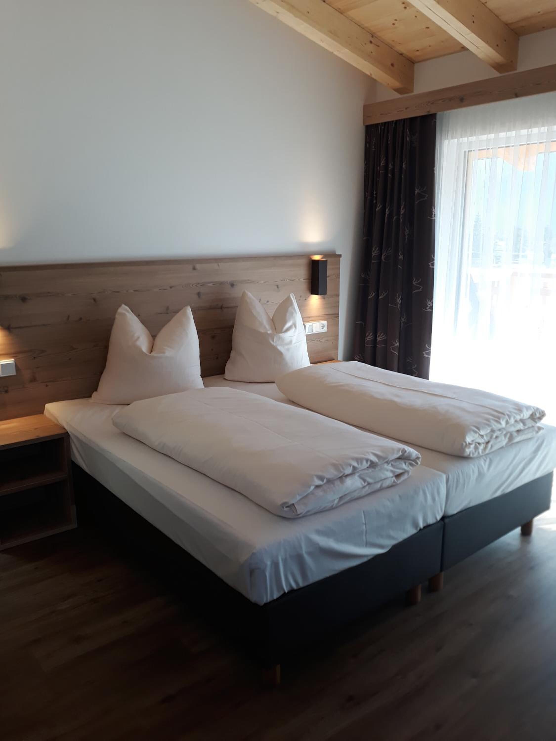 Una cama doble con cabecera de madera, dos mesitas de noche y una ventana con cortinas.