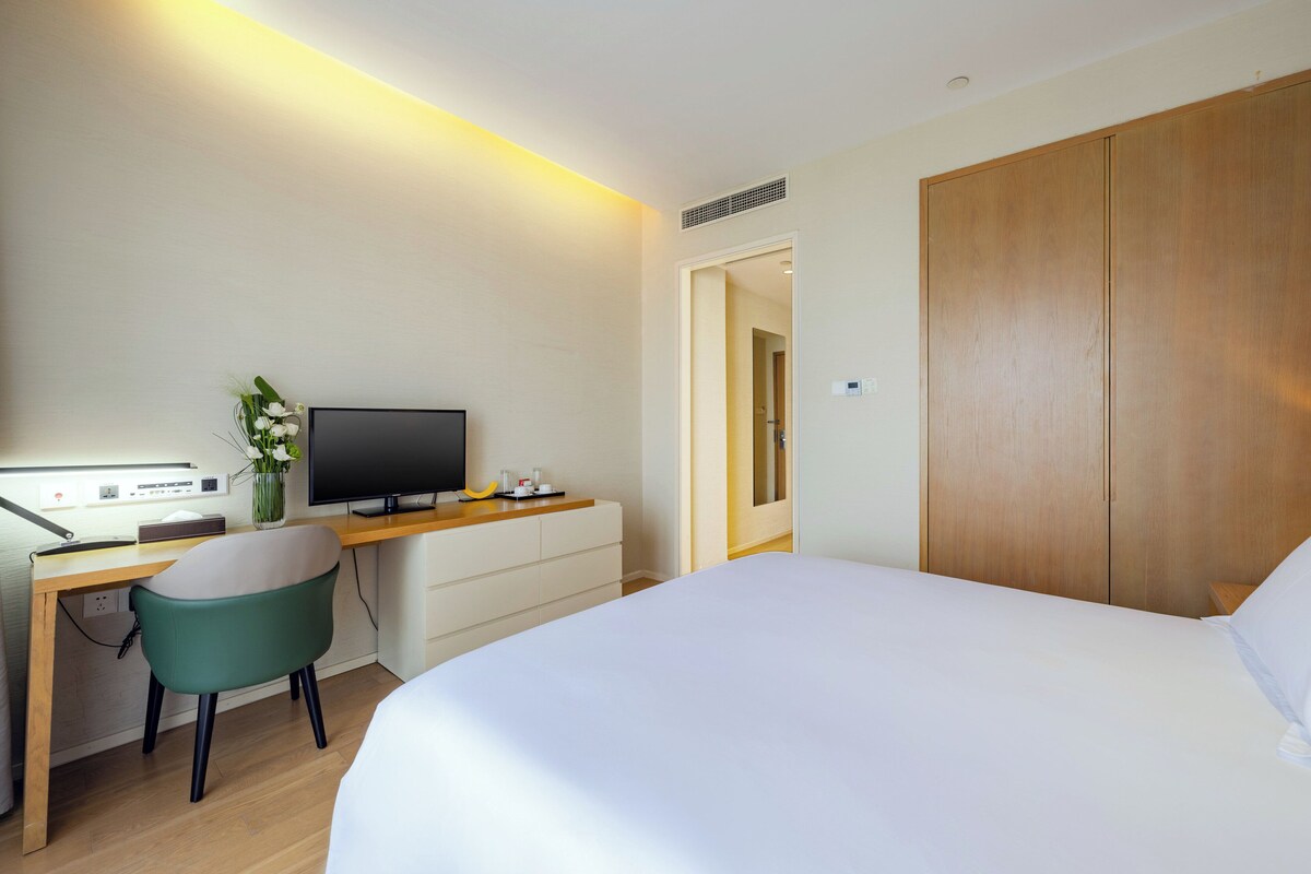 A hotel room with a bed, a desk with a computer, a chair, a TV, and a wardrobe.