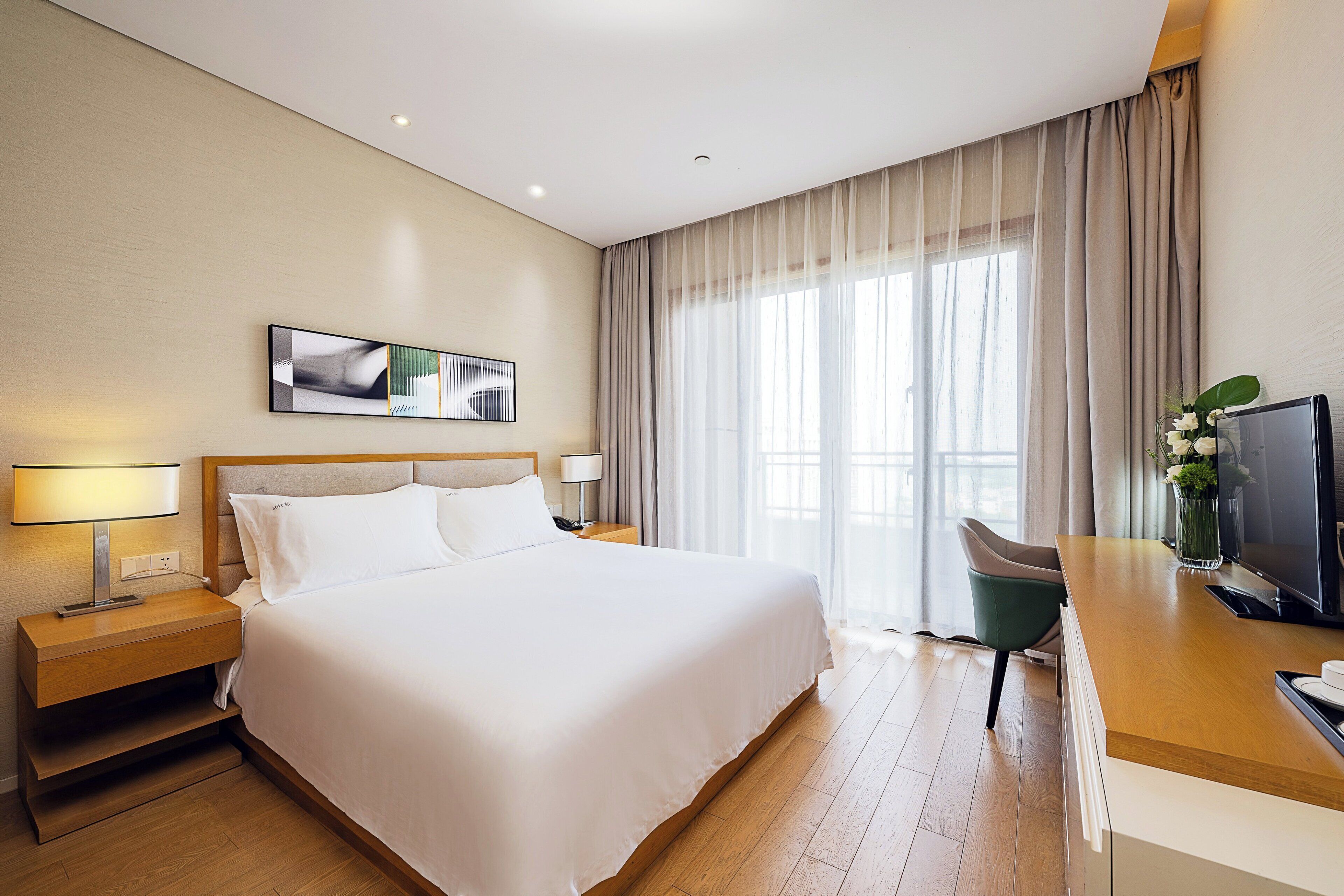 A hotel room with a large bed, a desk with a television, a nightstand, and a window with curtains.