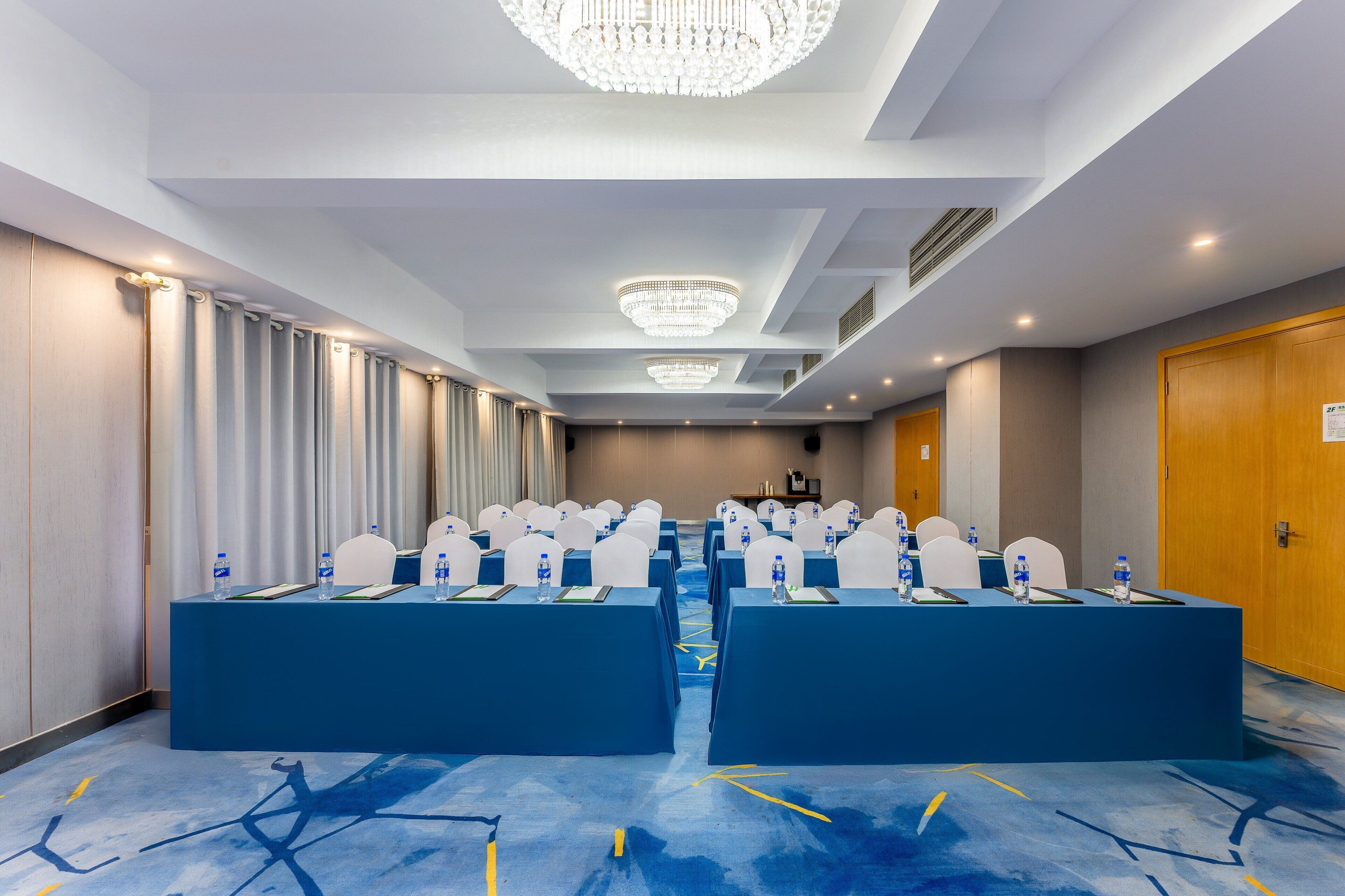 A conference room with blue tables, white chairs, and chandeliers.