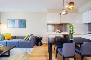 Ein modernes Wohnzimmer mit einer Couch, einem Esstisch und einer Küchenzeile mit Schränken und einem Herd.