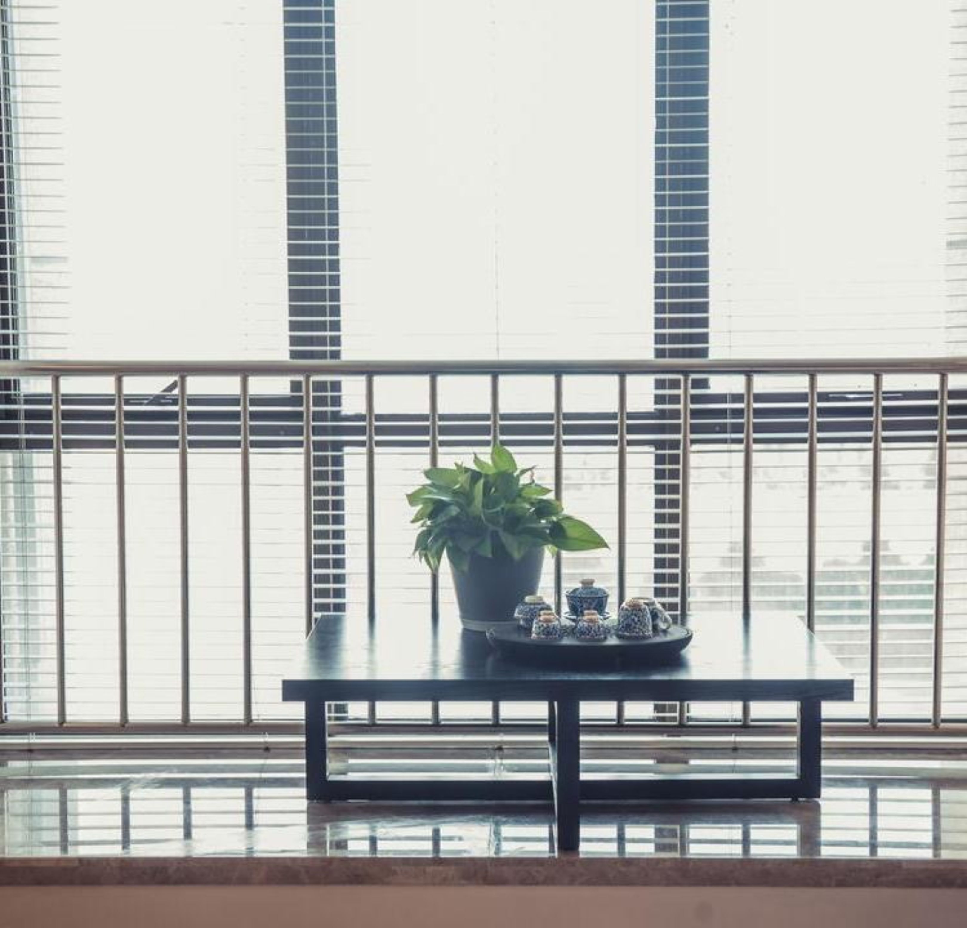 A balcony with a potted plant and a tray of tea cups.