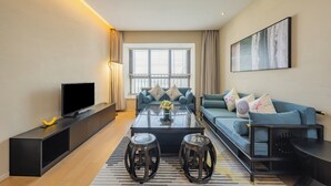 A modern living room with a sofa, coffee table, TV, and a painting on the wall. - Holiday Inn Hotel and Suites Suzhou Yangcheng Lake by IHG (Suzhou)