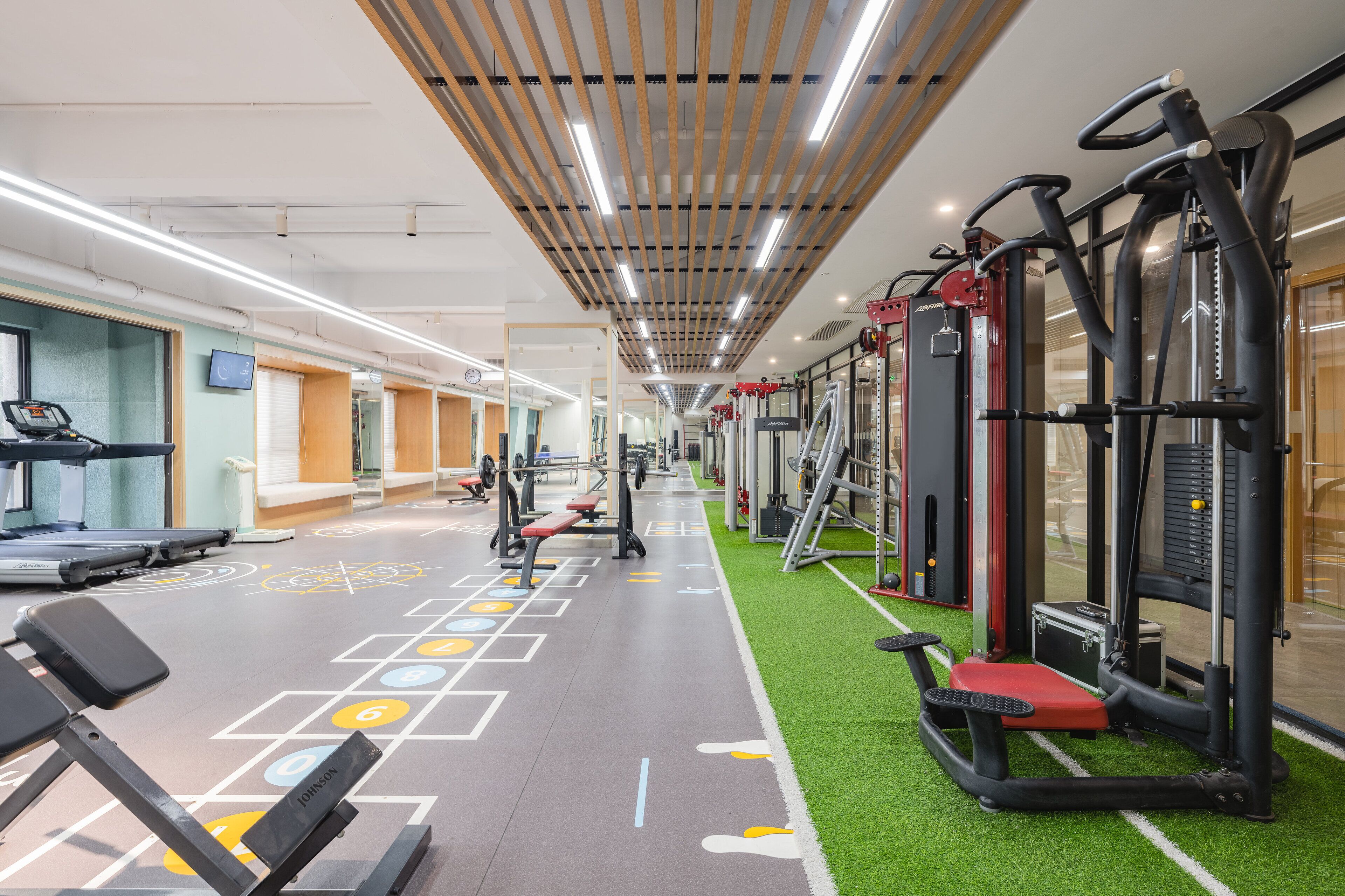 Une salle de sport équipée de tapis de course, d’appareils d’exercice et d’un espace recouvert d’une moquette verte.