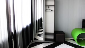 Una habitación con suelo a cuadros blancos y negros, un armario con espejo, un objeto cilíndrico verde y un perchero.