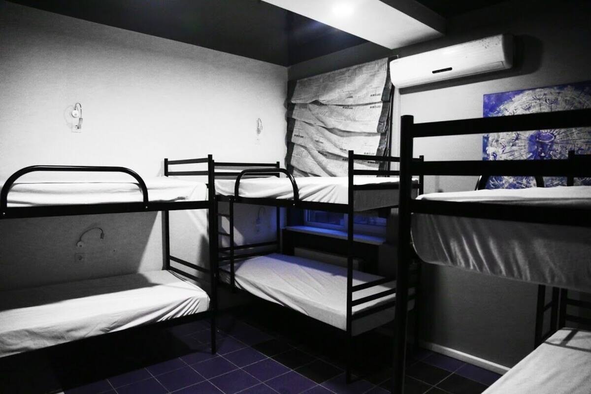 A dormitory room with bunk beds, a wall-mounted air conditioner, and a poster on the wall.
