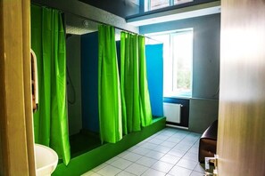 Casa de banho com cortinas de chuveiro verdes, uma pia branca e uma janela com vista para vegetação.