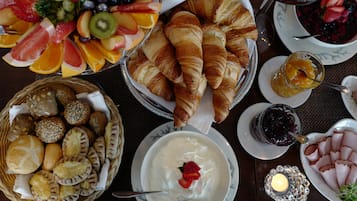 Pöydällä on croissantteja, kulhossa jogurttia ja mansikka, kori täynnä leivonnaisia sekä lautanen viipaloitua kinkkua.