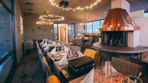 A restaurant with long communal tables, a large wood-burning stove, and string lights on the ceiling. - Little Peak (Kuusamo)