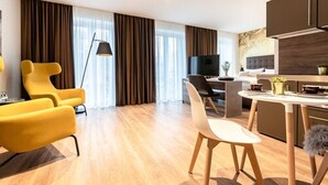 A modern hotel room with a dining area, a sofa, a TV, and a kitchen area. - H23 Boardinghotel (Stuttgart)