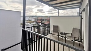 A balcony with a view of a cityscape, featuring a metal railing, two chairs, a small table, and a white wall. - H23 Boardinghotel (Stuttgart)