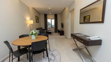 A modern hotel room with a dining area, a desk with a mirror, and a view of the outdoors.