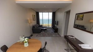 Une chambre d’hôtel moderne dotée d’un coin repas, d’un canapé, d’une télévision et offrant une vue sur la mer.