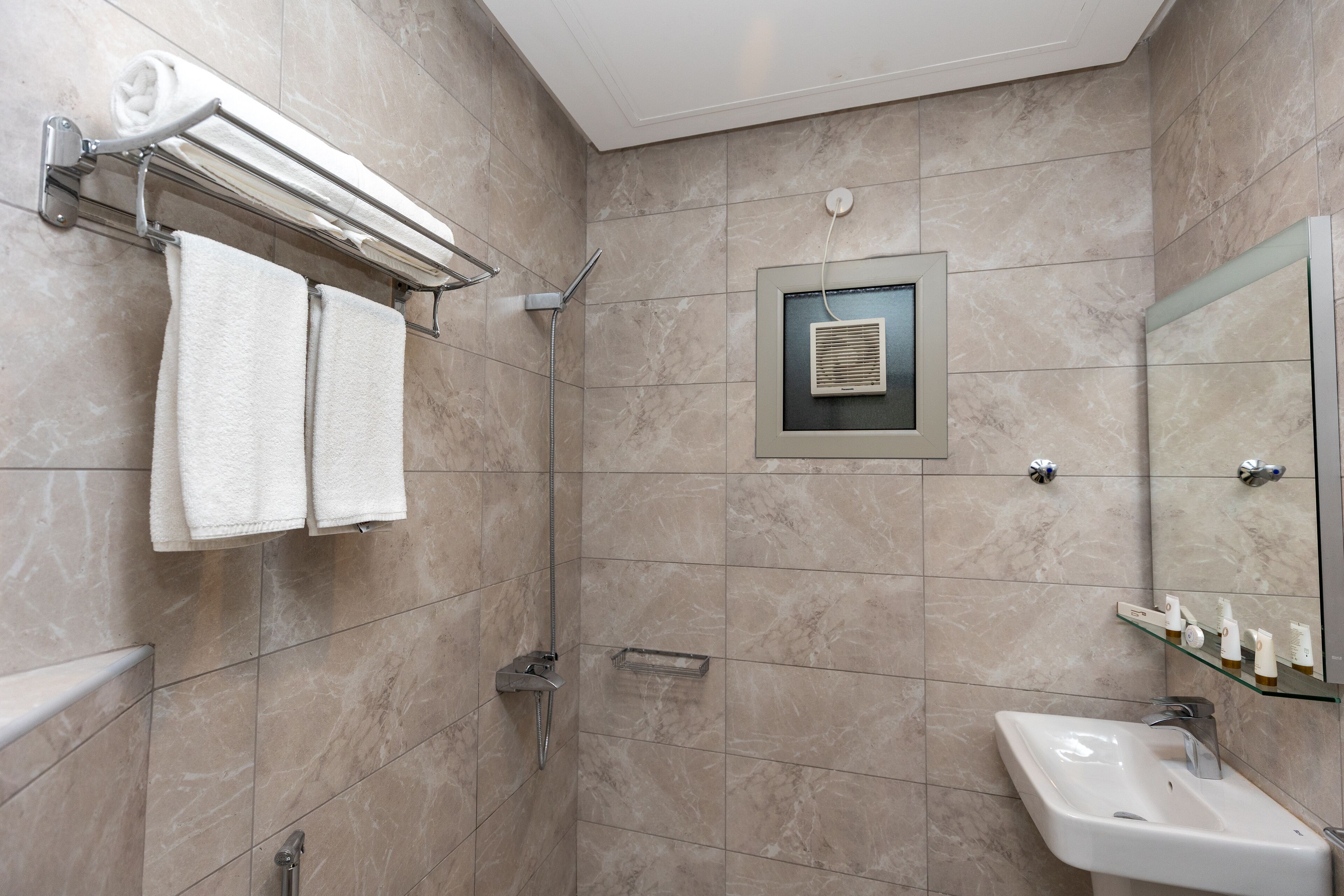 Een moderne badkamer met een inloopdouche, een glazen plankje met toiletartikelen en een grote spiegel.