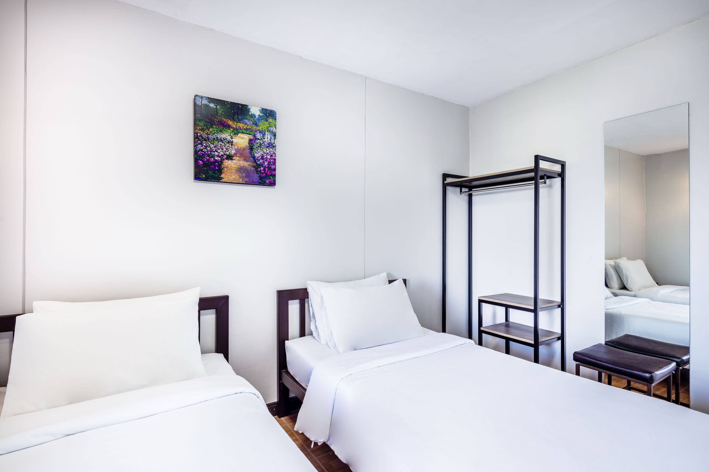 A hotel room with two beds, a large mirror, a painting on the wall, and a small table.