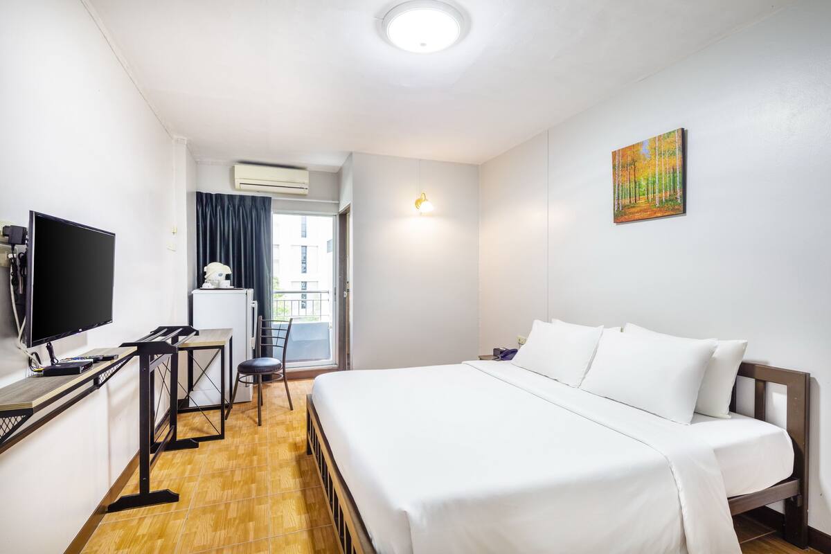 Hotellihuone, jossa on sänky, työpöytä tietokoneella, televisio ja ikkuna, jossa on verhot.