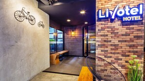 A modern hotel lobby with a brick wall, a bicycle art installation, a wooden bench, and a black chair.
