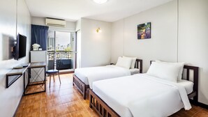 A hotel room with two beds, a desk with a chair, a TV, and a balcony with a view of buildings.