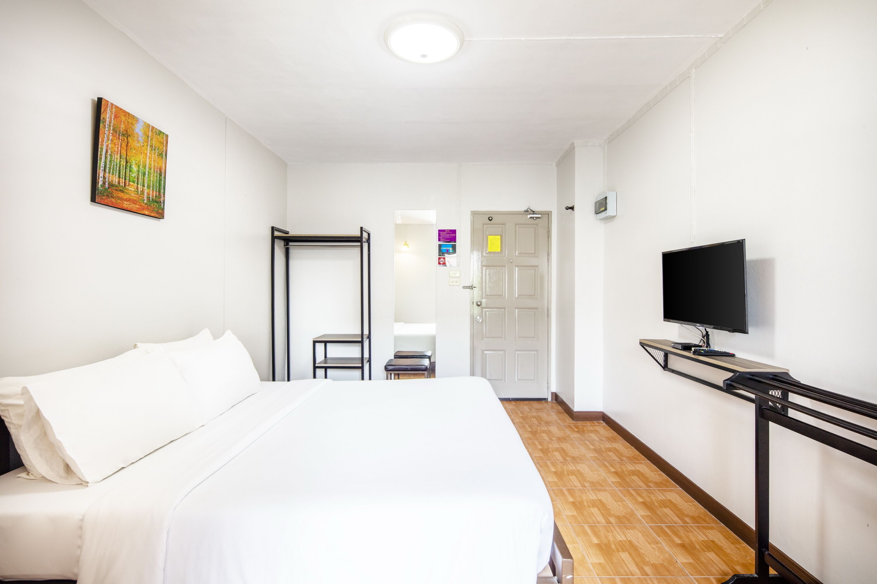 A hotel room with a bed, a television, a painting, and a door leading to another room.