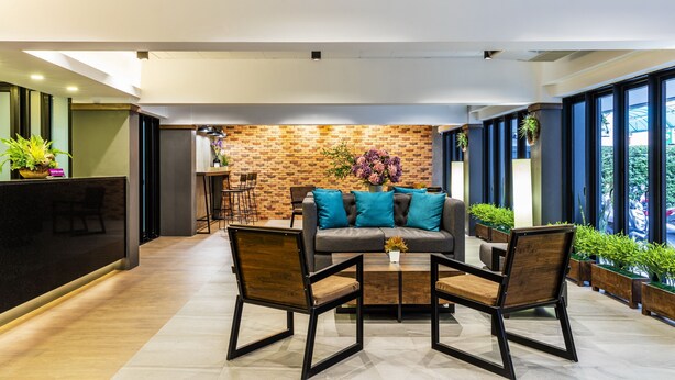 A modern interior with a reception desk, a brick accent wall, a sofa with teal cushions, and a coffee table. - Livotel Express Hotel Ramkhamhaeng 50  Bangkok (Bangkok)