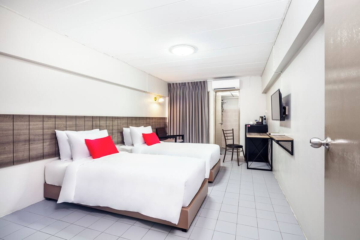 A hotel room with two beds, a desk, a chair, a TV, and a bathroom visible through an open door.