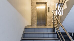 A modern elevator with a metallic finish, flanked by a staircase with metal railings and tiled steps. - Livotel Express Hotel Ramkhamhaeng 50  Bangkok (Bangkok)