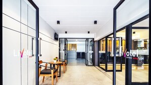 A hotel corridor with glass doors, wooden chairs, and a tiled floor. - Livotel Express Hotel Ramkhamhaeng 50  Bangkok (Bangkok)