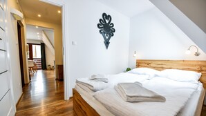 A bedroom with a wooden headboard, a neatly made bed with white linens, and a decorative wall piece. - Rentplanet - Bulwary Słowackiego (Zakopane)